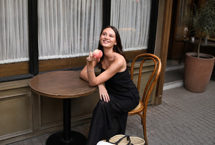 Woman in a black dress seated at a cafe table holding a peach